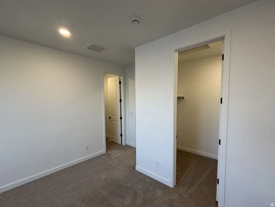 Unfurnished bedroom featuring a spacious closet, dark carpet, and recessed lighting