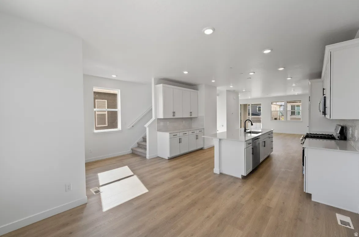 Kitchen featuring white cabinetry, a center island with sink, decorative backsplash, open floor plan, and light wood-style flooring