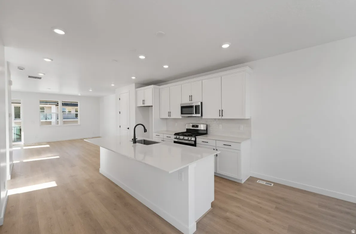 Kitchen with white cabinetry, an island with sink, appliances with stainless steel finishes, backsplash, and light stone countertops