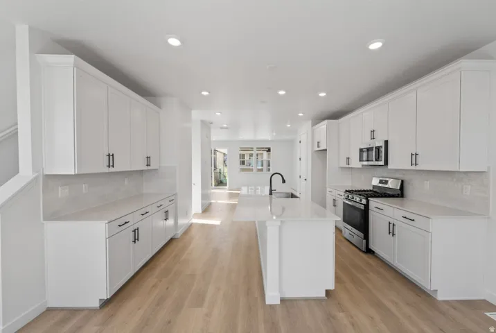 Kitchen featuring backsplash, appliances with stainless steel finishes, white cabinets, a center island with sink, and recessed lighting