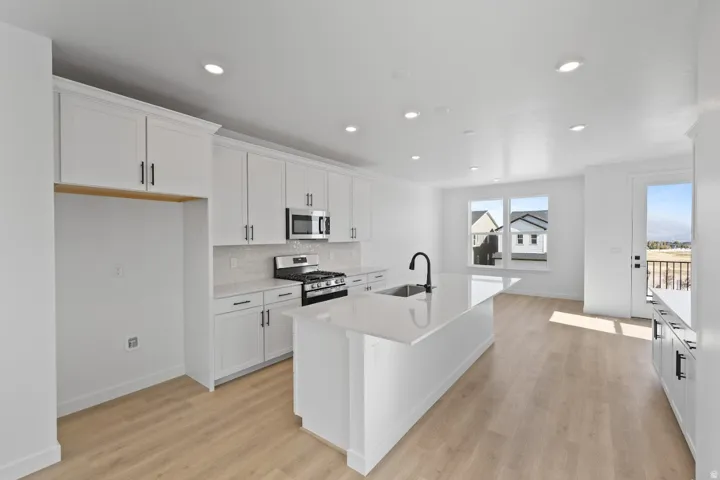 Kitchen with white cabinetry, appliances with stainless steel finishes, a kitchen island with sink, light wood finished floors, and recessed lighting