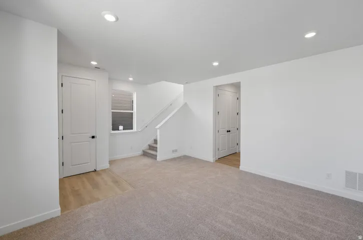 Below grade area with stairway, light colored carpet, recessed lighting, and light wood-style flooring