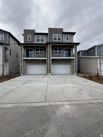 View of front facade featuring a balcony, driveway, and a garage