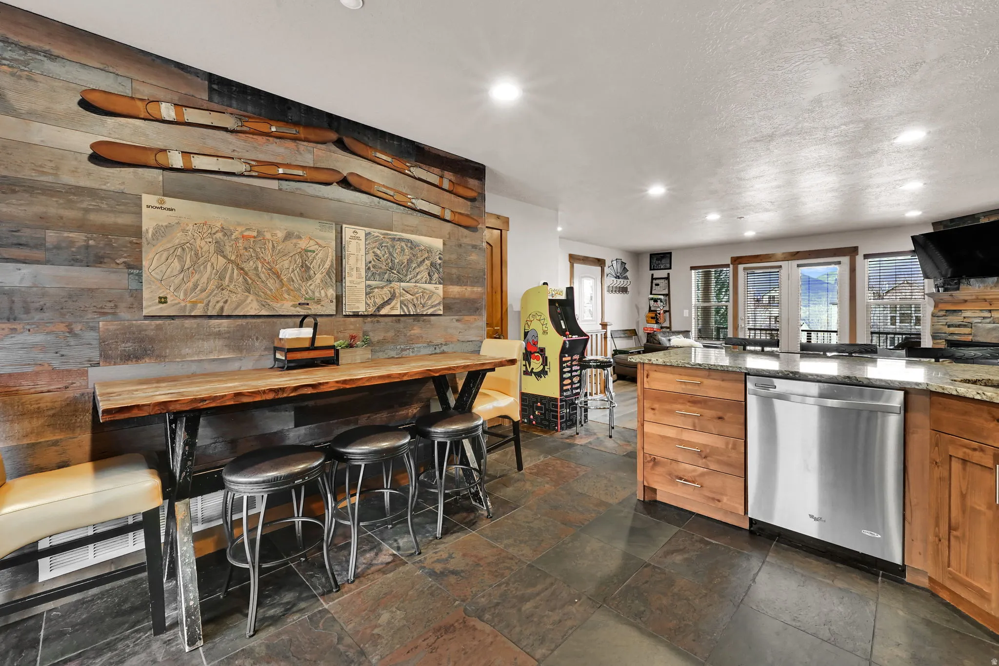 Kitchen featuring stainless steel dishwasher, light stone countertops, recessed lighting, brown cabinetry, and stone tile floors