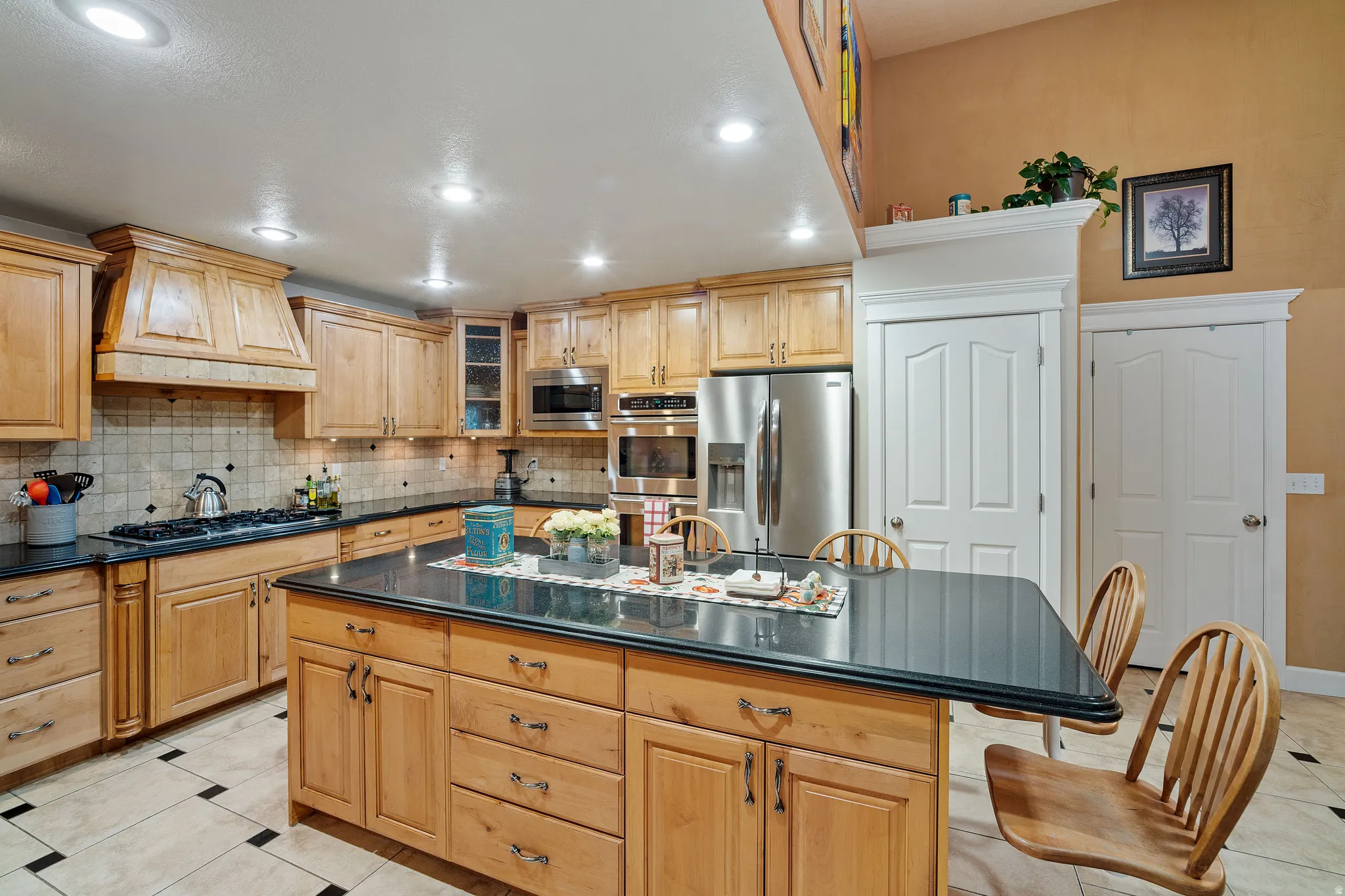 Kitchen featuring light tile patterned floors, appliances with stainless steel finishes, glass insert cabinets, a kitchen island, and tasteful backsplash