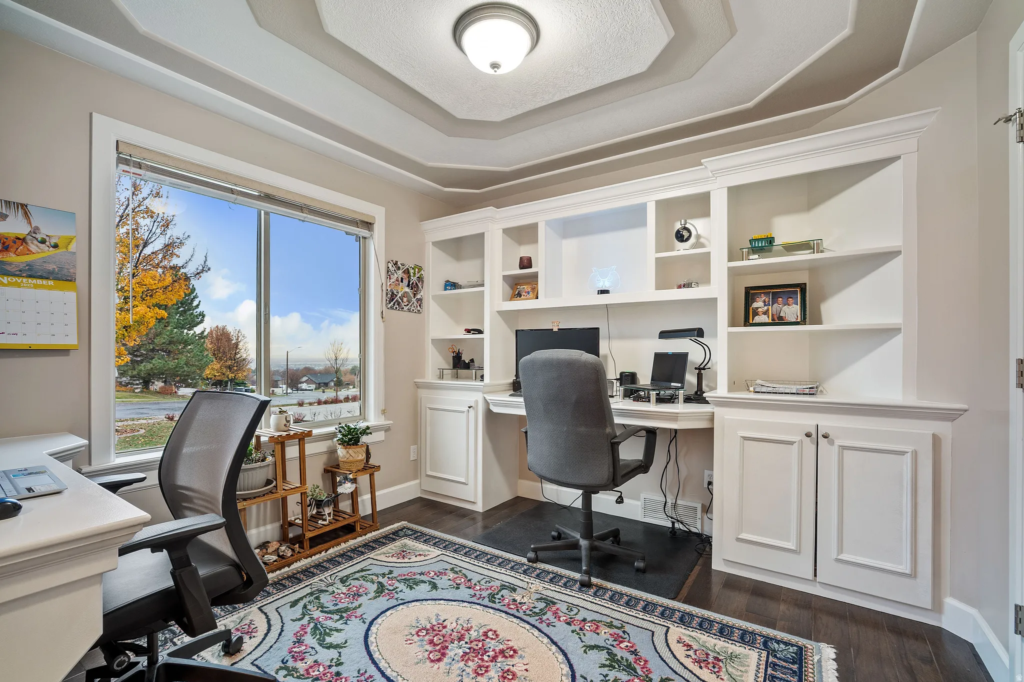 Office area with dark wood-style floors, built in study area, and a raised ceiling