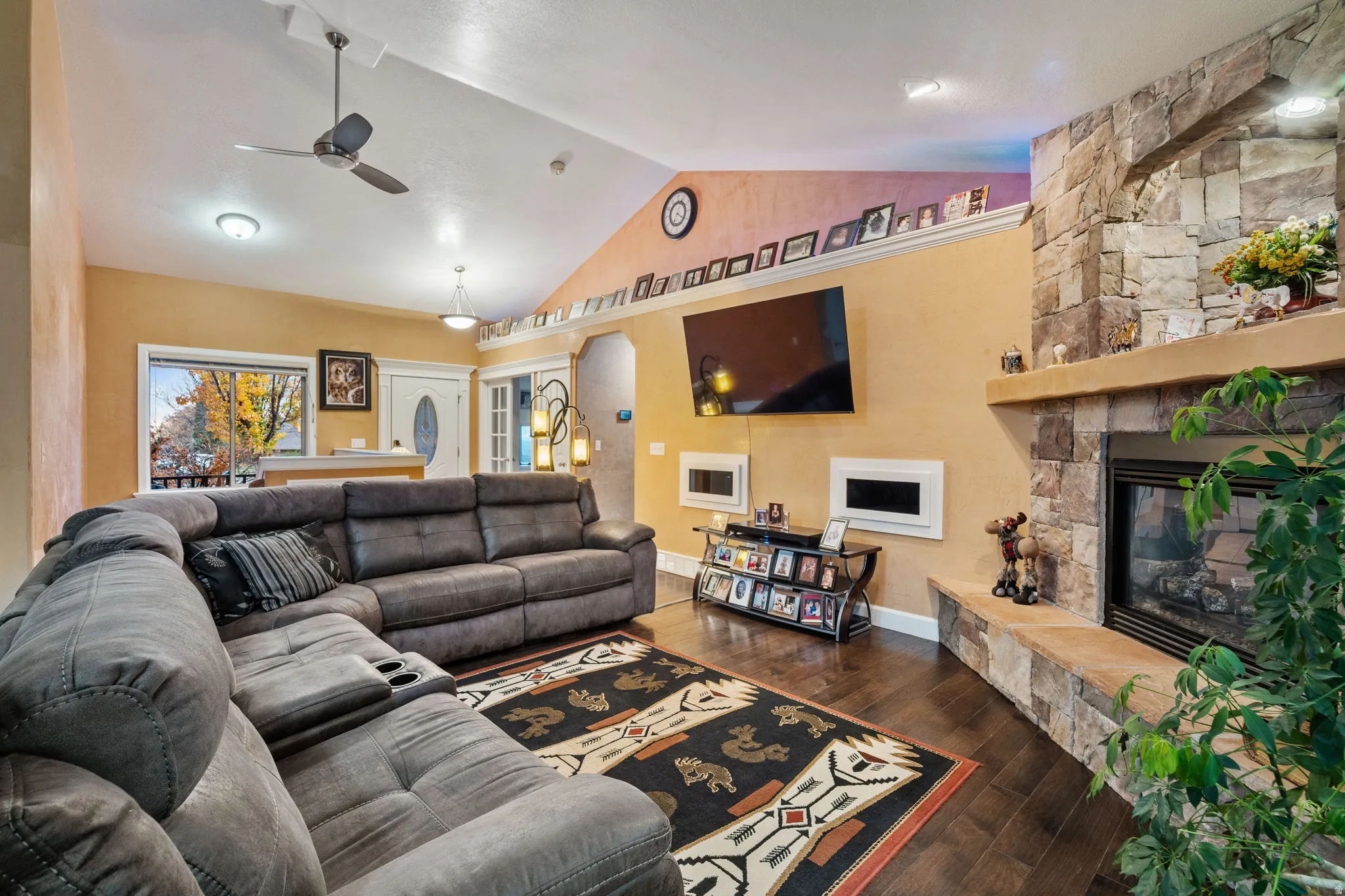 Living room with vaulted ceiling, dark wood-type flooring, a ceiling fan, and a fireplace