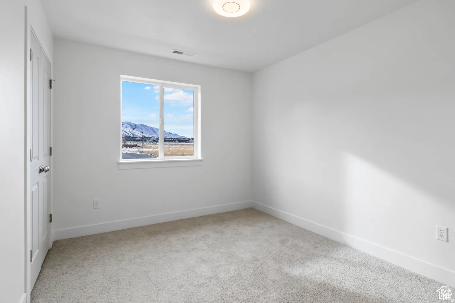 Empty room featuring a mountain view and light carpet