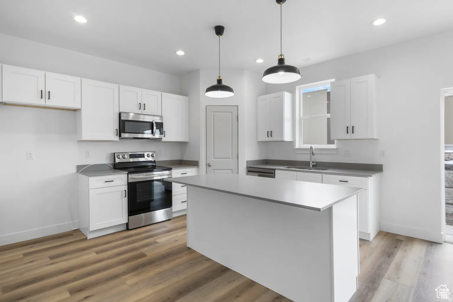 Kitchen featuring stainless steel appliances, white cabinets, decorative light fixtures, a center island, and light wood-type flooring