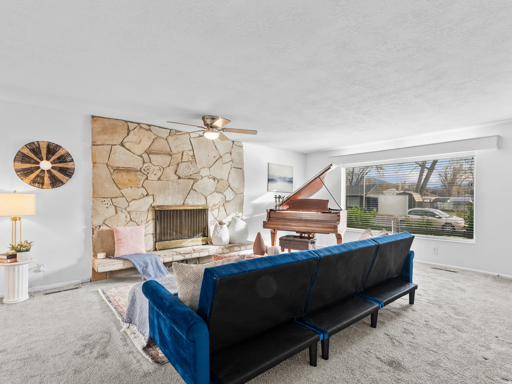 Carpeted living room with a stone fireplace, a ceiling fan, and a textured ceiling