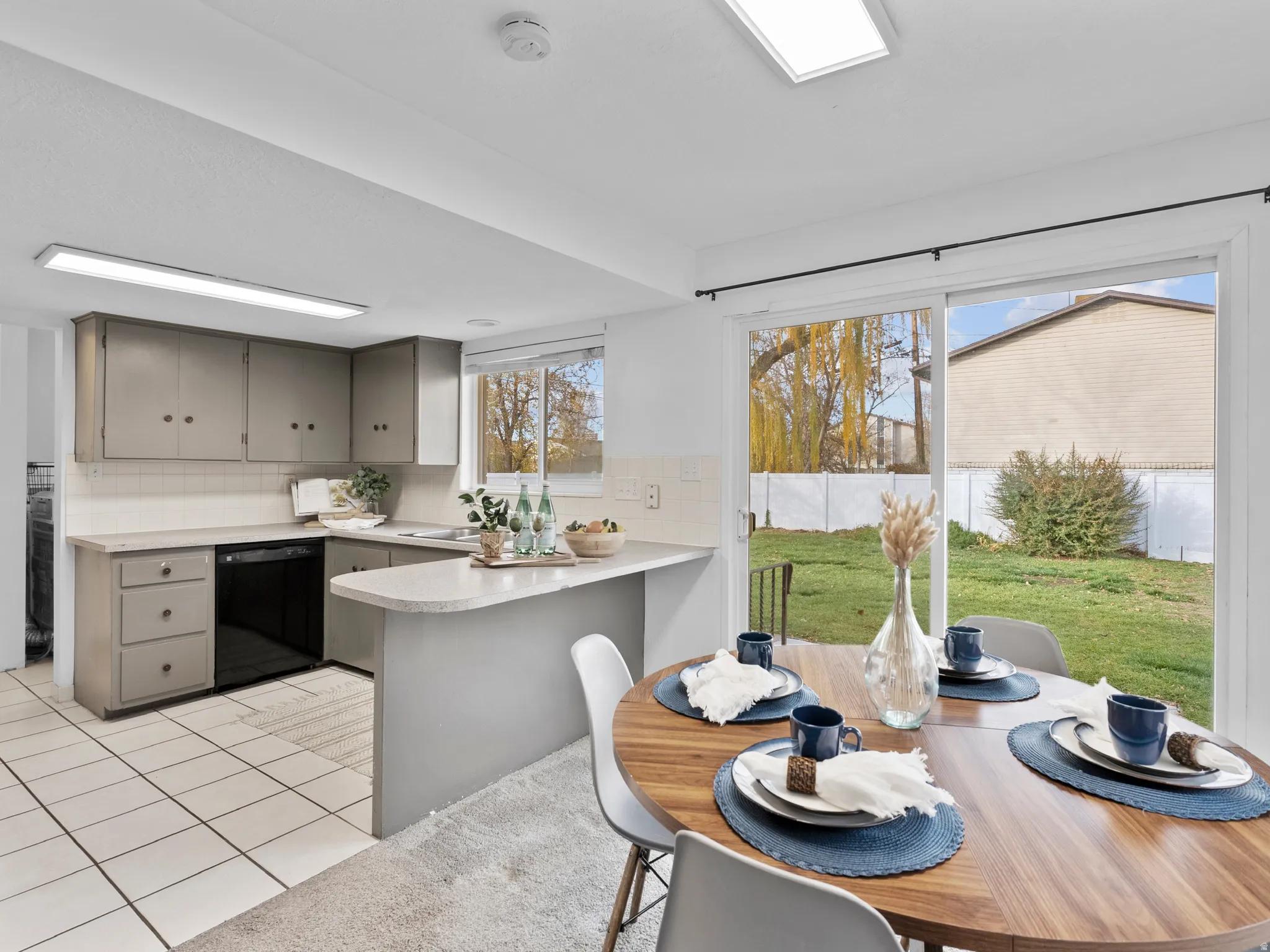 Kitchen featuring gray cabinets, a peninsula, light countertops, black dishwasher, and tasteful backsplash