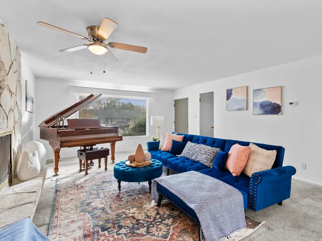 Carpeted living room featuring a stone fireplace and a ceiling fan