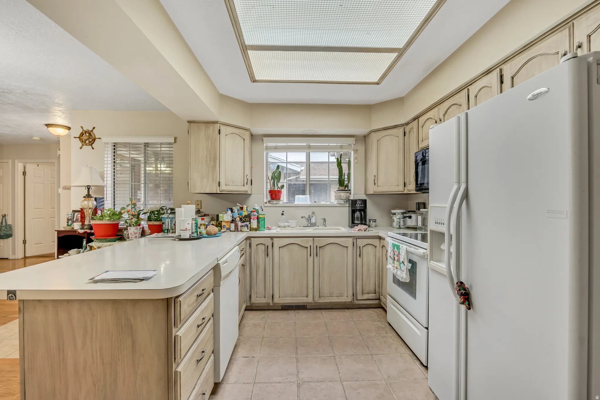 Kitchen featuring white appliances, light brown cabinets, a peninsula, and light countertops