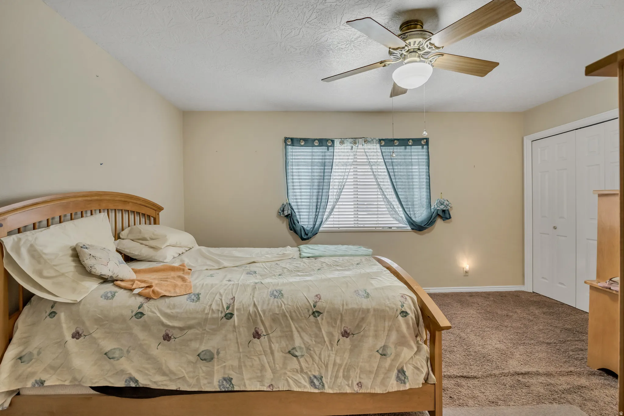 Carpeted bedroom with ceiling fan, a textured ceiling, and a closet