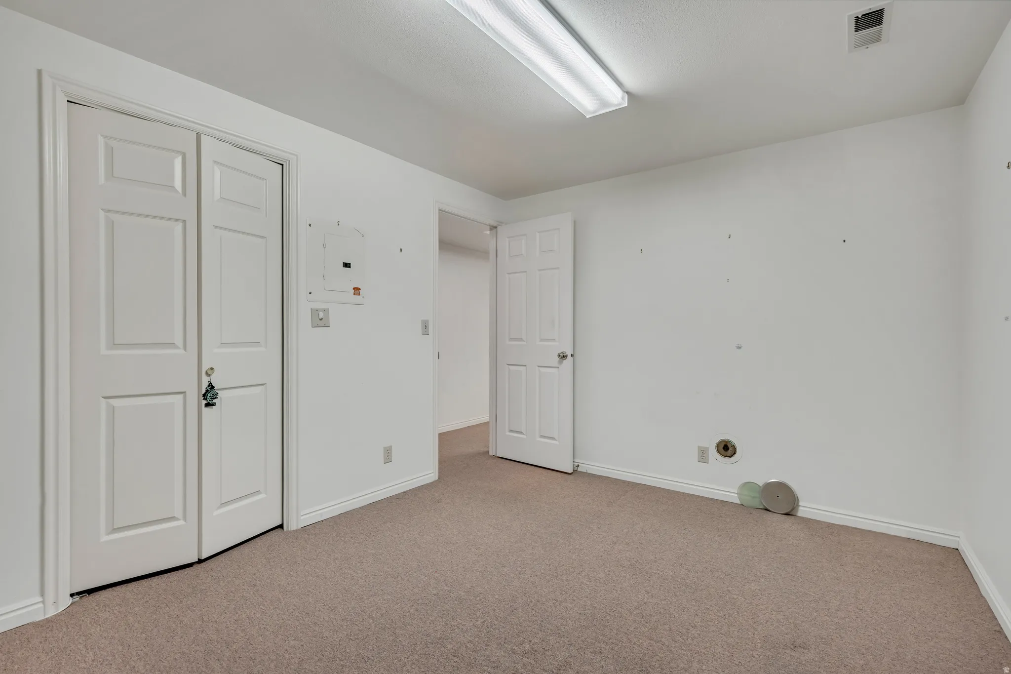 Unfurnished bedroom with light carpet, electric panel, and a closet