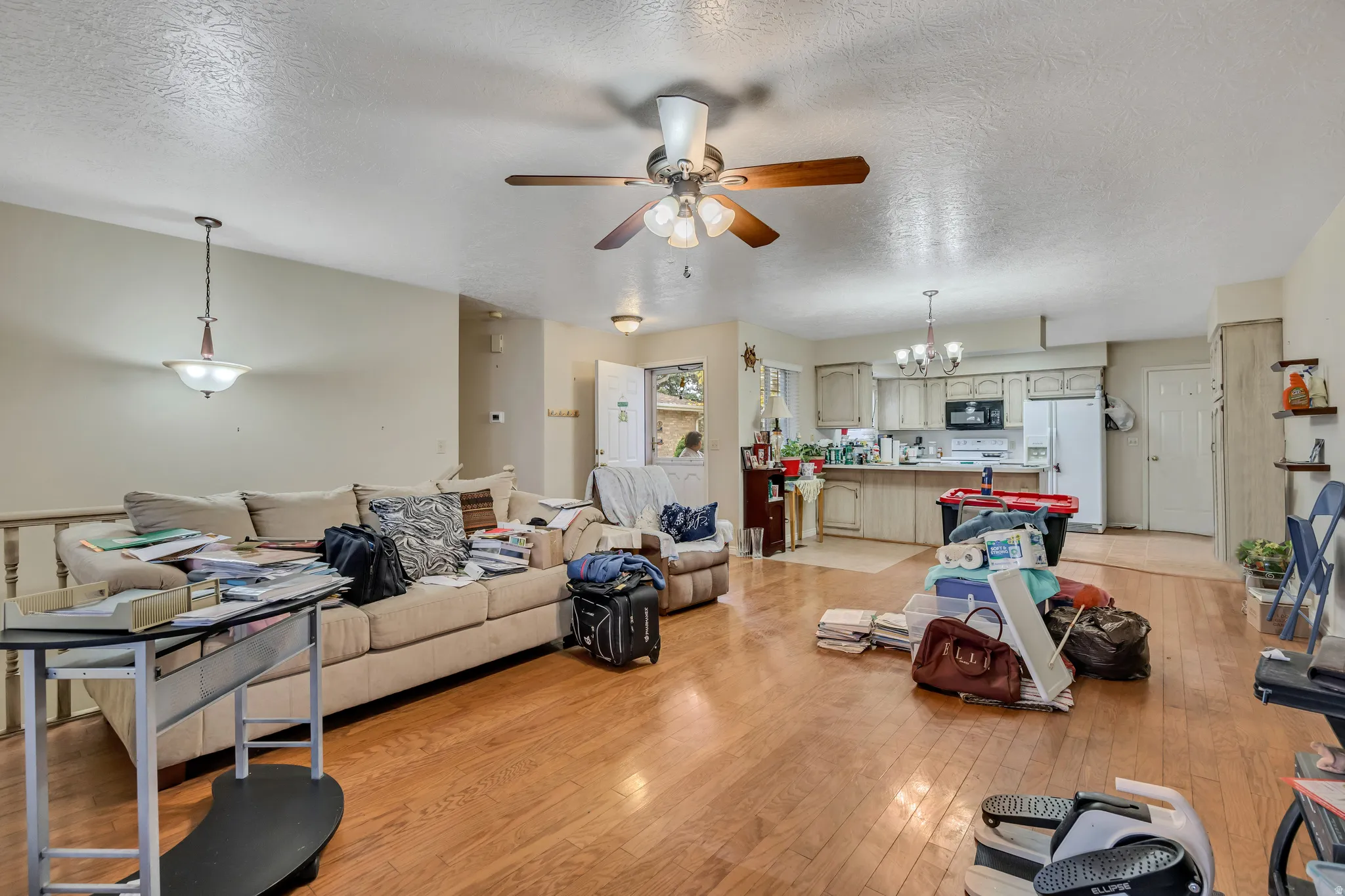 Living area featuring a textured ceiling, light wood-style floors, ceiling fan, and a chandelier