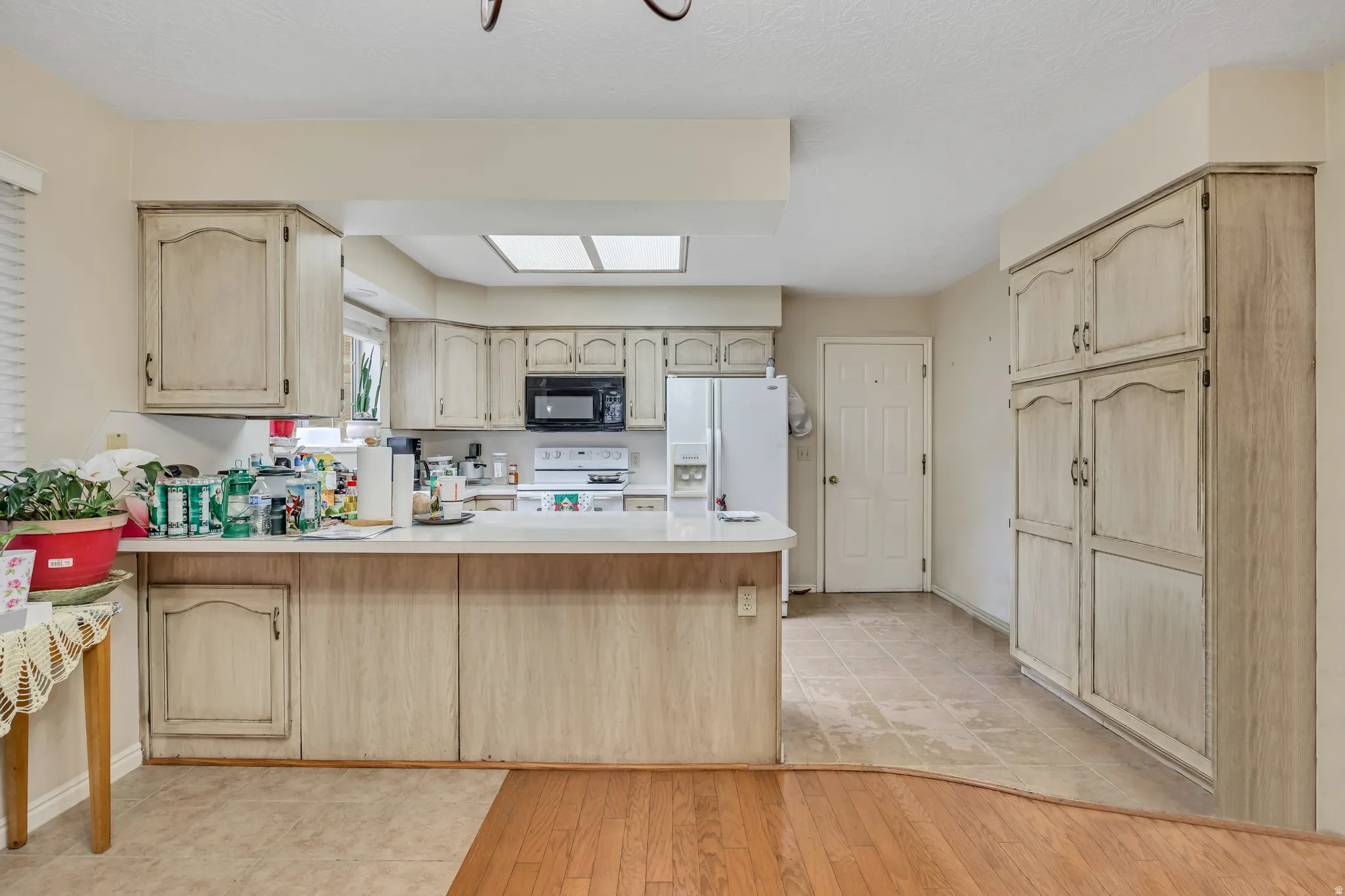 Kitchen featuring light brown cabinetry, a peninsula, light countertops, light wood-style flooring, and white appliances