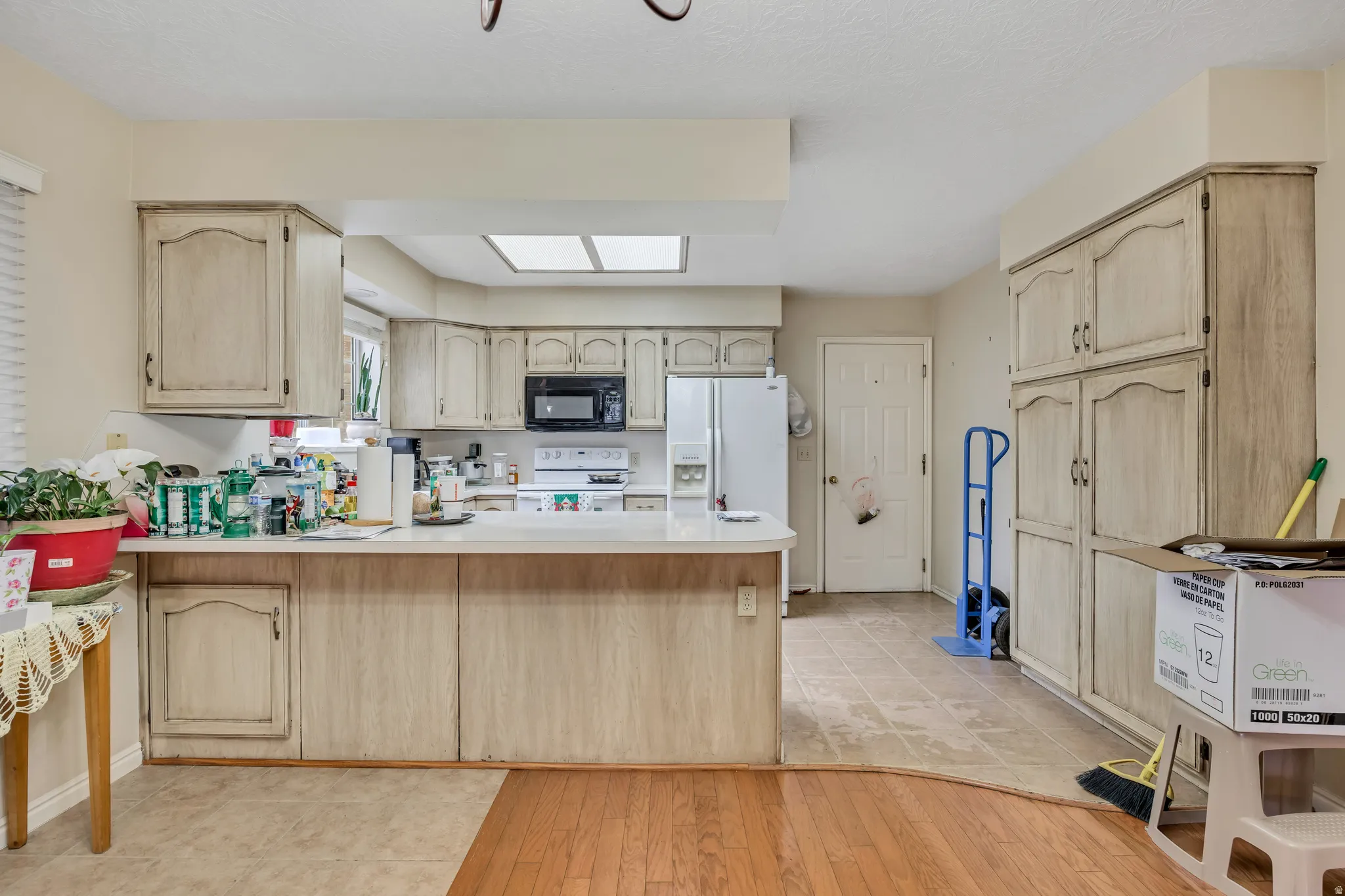 Kitchen with light brown cabinetry, a peninsula, light countertops, light wood-style floors, and white appliances