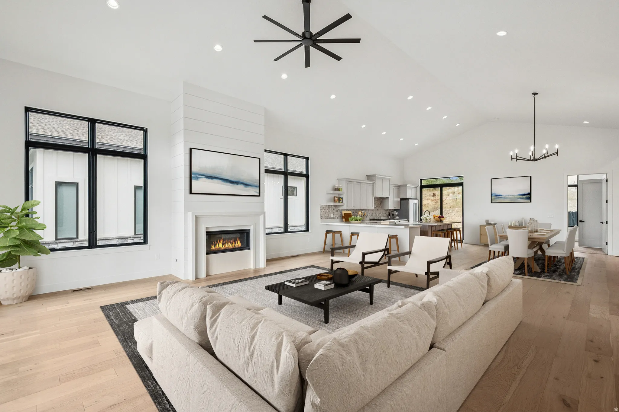 Upper level great room featuring a glass covered gas fireplace, light wood finished floors, high vaulted ceiling, recessed lighting, and ceiling fan (virtual staging)