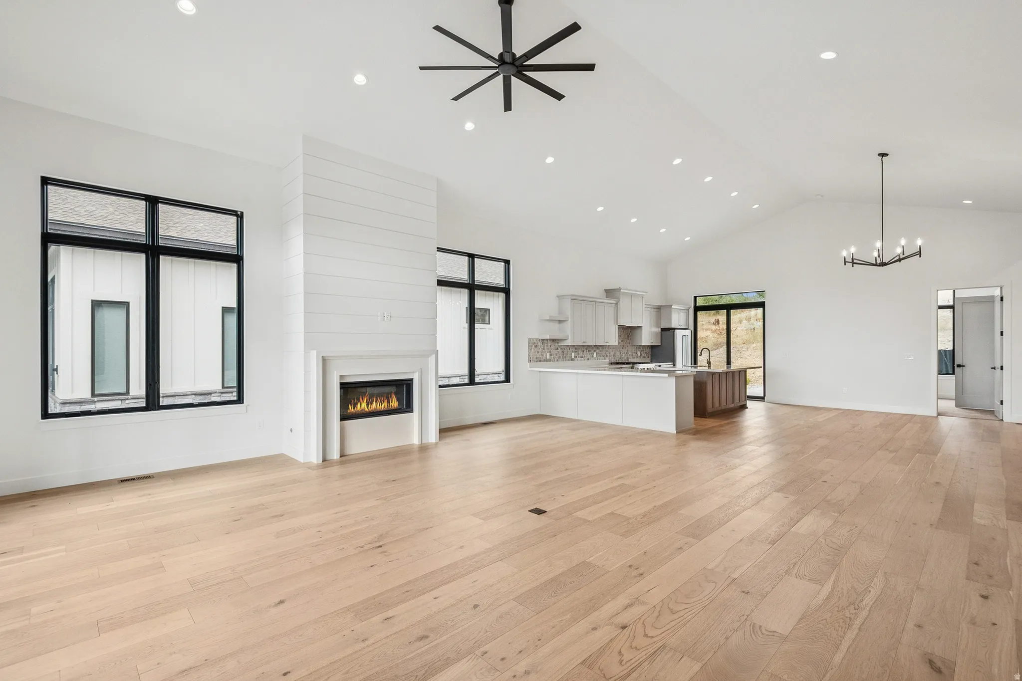 Upper level great room featuring a glass covered gas fireplace, light wood finished floors, high vaulted ceiling, recessed lighting, and ceiling fan