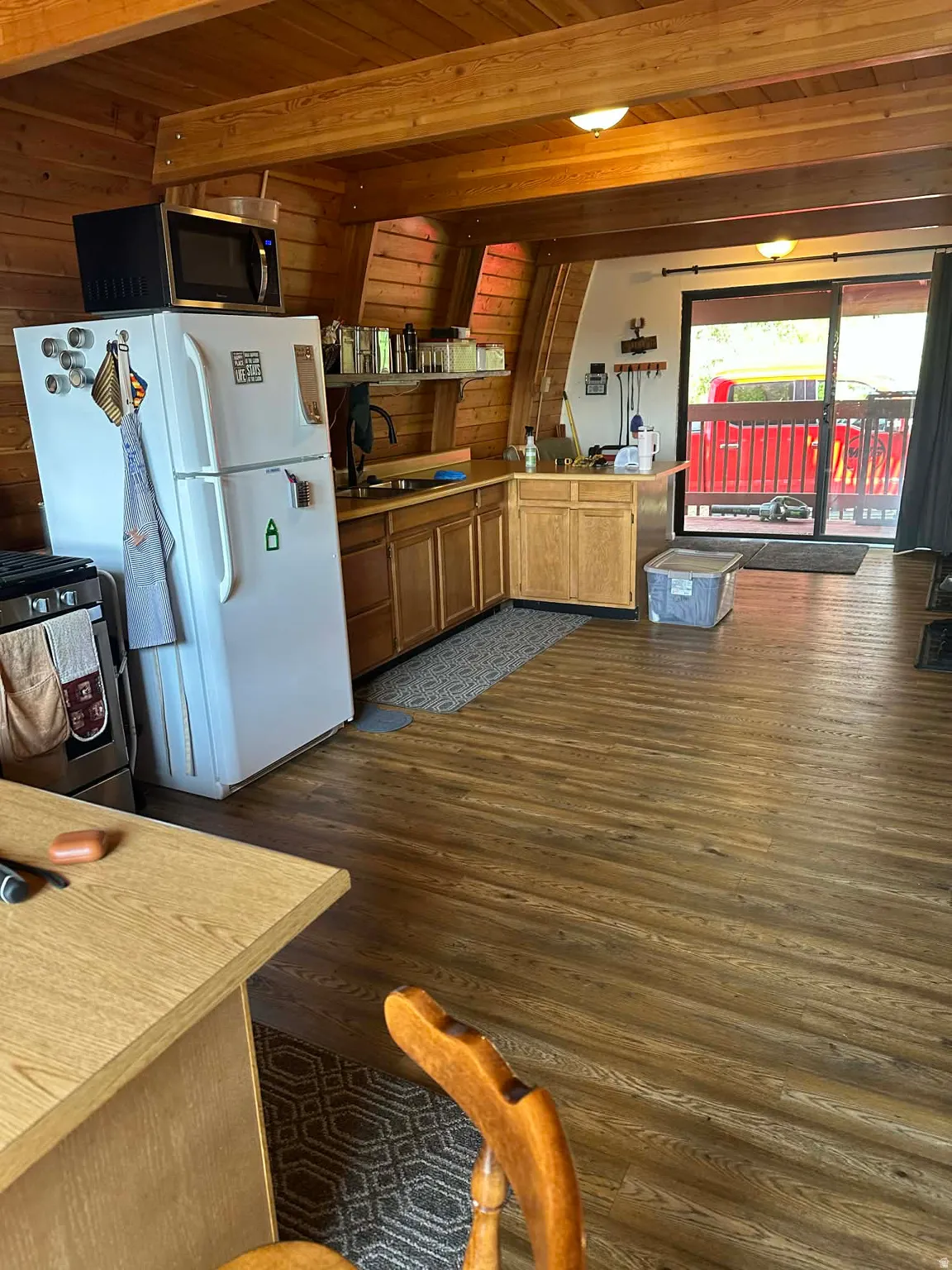 Kitchen featuring light countertops, stainless steel range with gas cooktop, dark wood-style flooring, a wooden ceiling with exposed beams, and a peninsula