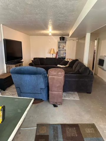 Living area with a textured ceiling, heating unit, and concrete flooring