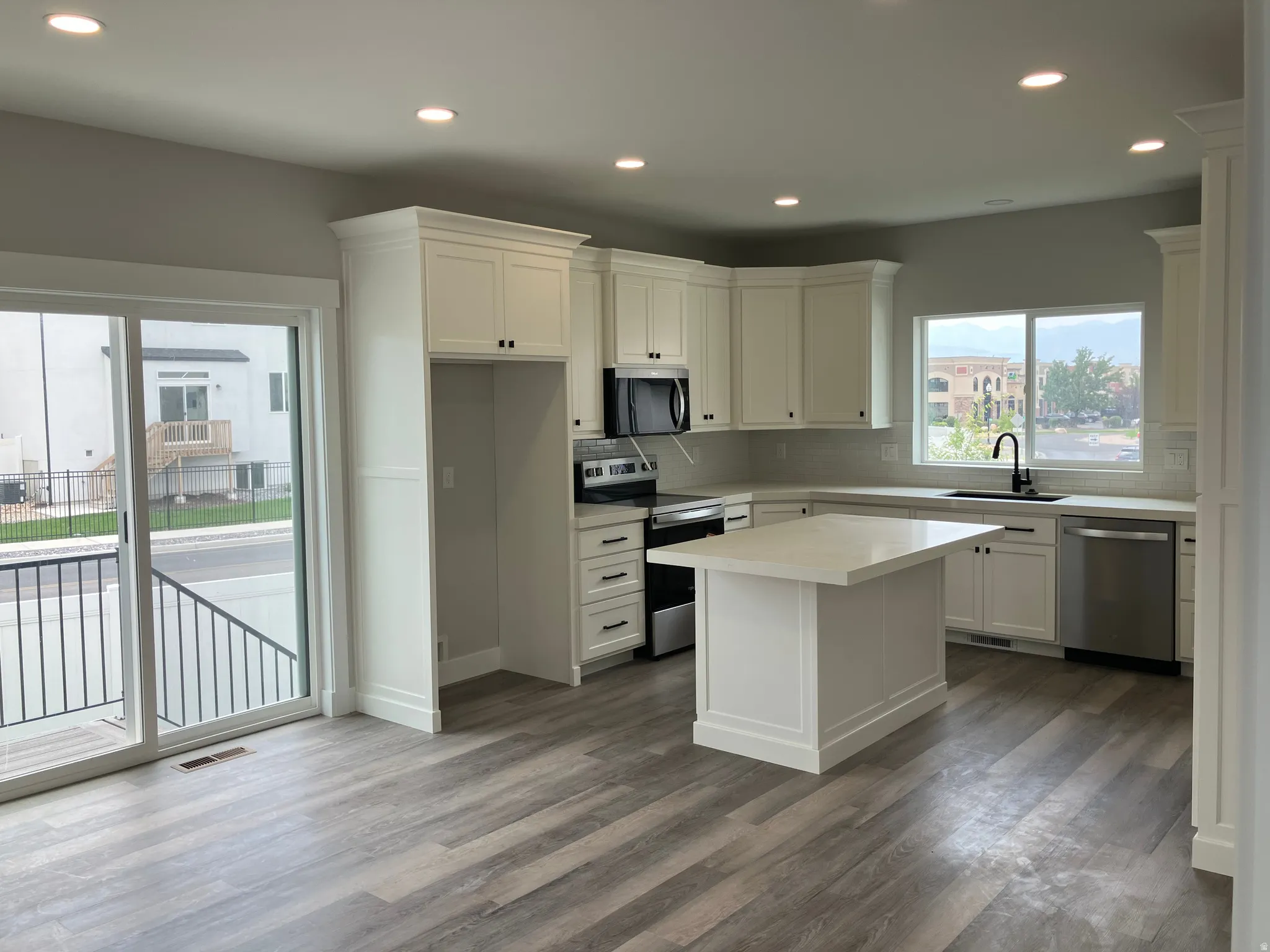 Modern kitchen featuring cream cabinetry, stainless steel appliances, quartz countertops, a central island with prep space, and wood-finish flooring throughout