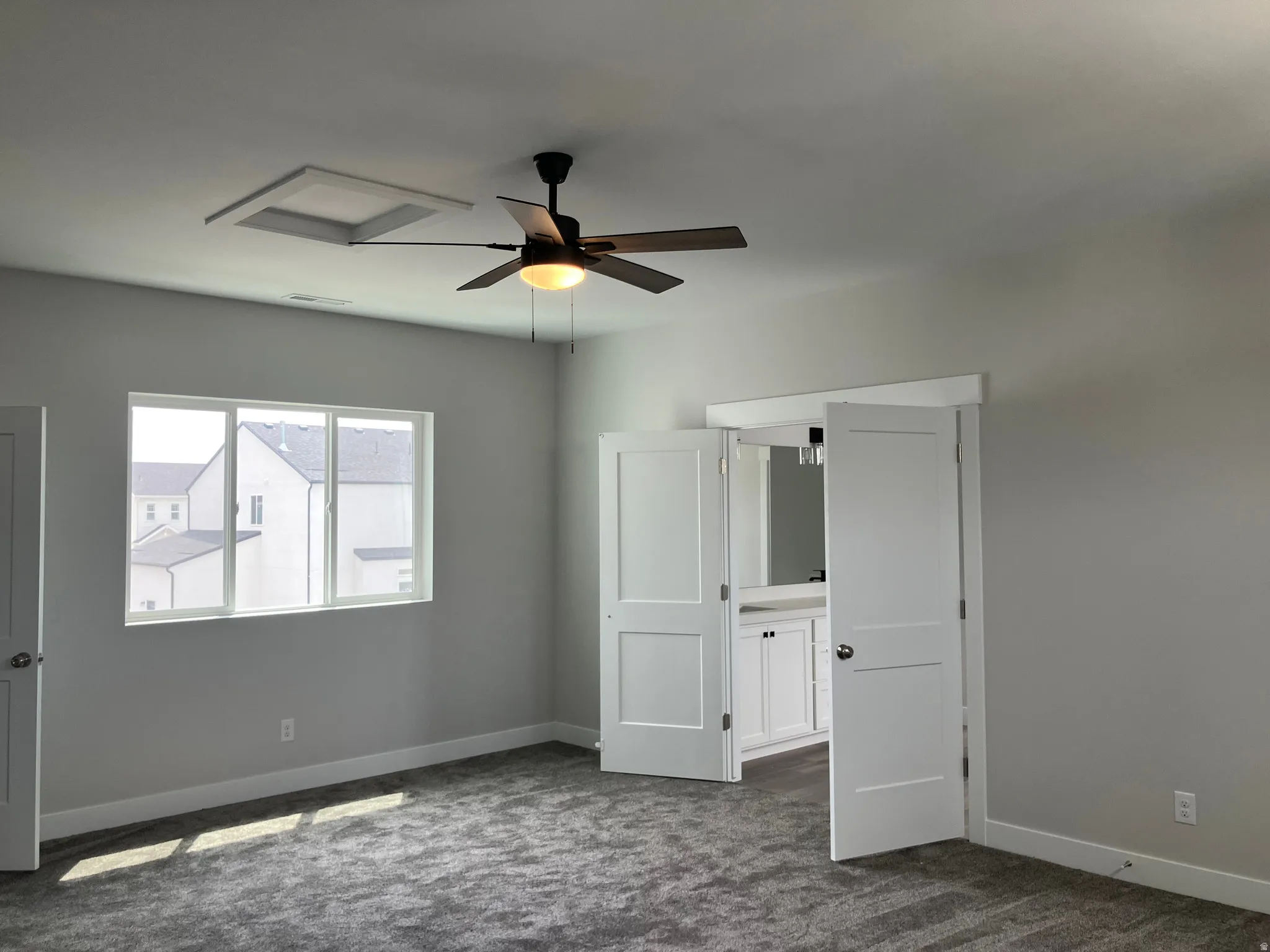 Bright corner bedroom with dual windows flooding the space with natural light, neutral gray walls, carpeted flooring, ceiling fan with integrated lighting, and white six-panel doors providing access to adjoining spaces