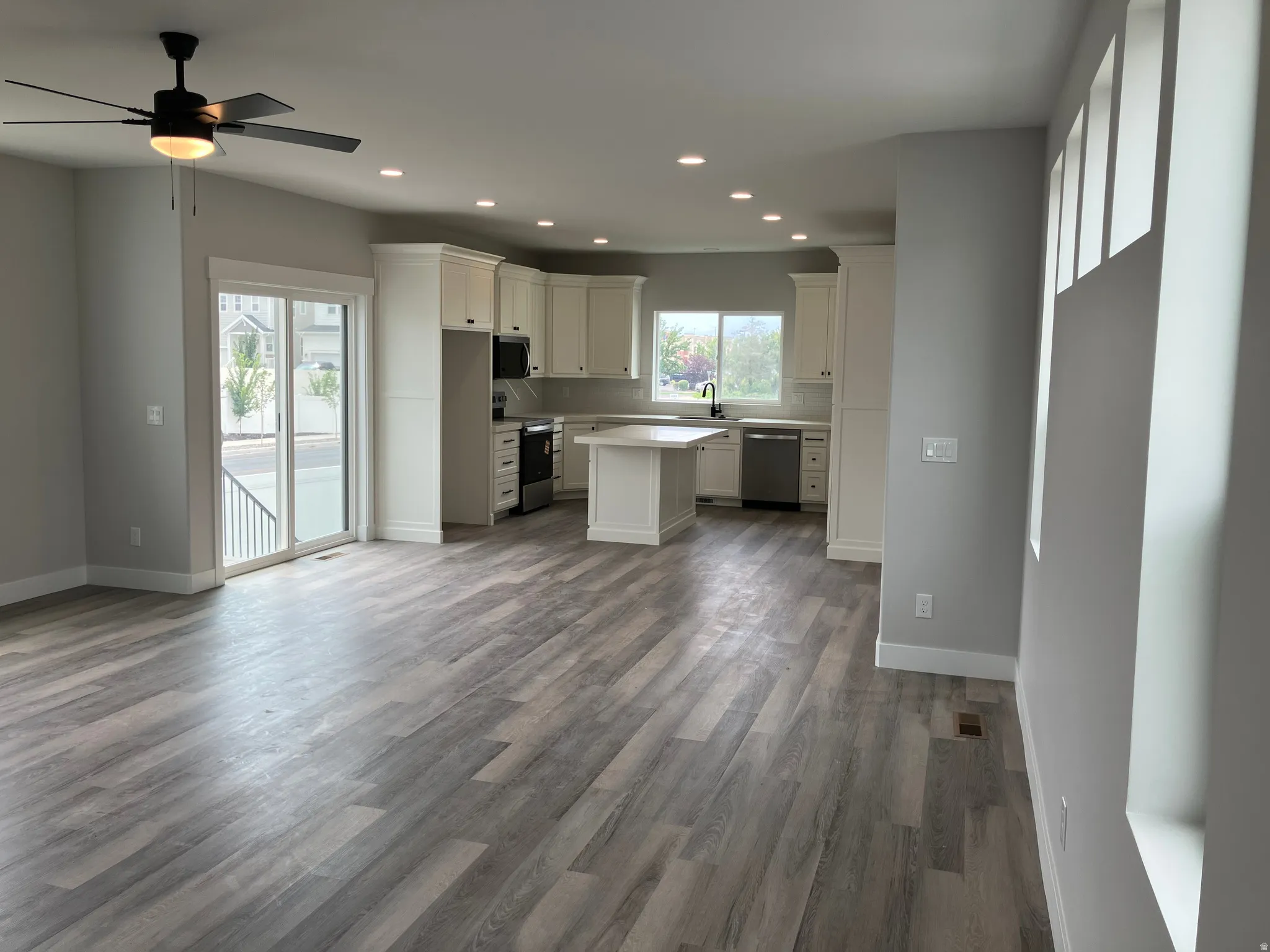 Open-concept living and kitchen area featuring wood-finish flooring throughout, recessed ceiling lighting, a ceiling fan with integrated light fixture, and a centered kitchen island