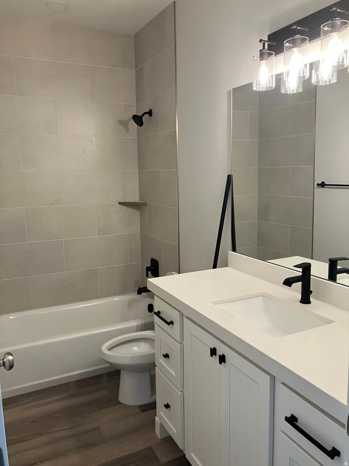 Bathroom with wood-finish flooring, a white vanity with a recessed sink, a white countertop, and a shower/tub combination with light-colored tile surround