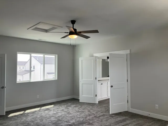 Bright corner bedroom with dual windows flooding the space with natural light, neutral gray walls, carpeted flooring, ceiling fan with integrated lighting, and white six-panel doors providing access to adjoining spaces