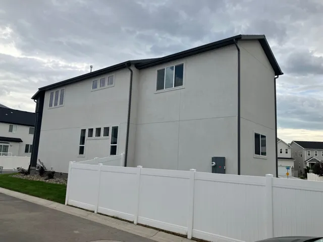 Contemporary stucco exterior featuring a white vinyl privacy fence, dark roof, dark gutters, and multiple window configurations
