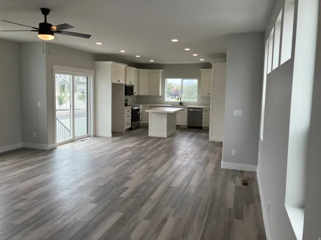 Open-concept living and kitchen area featuring wood-finish flooring throughout, recessed ceiling lighting, a ceiling fan with integrated light fixture, and a centered kitchen island
