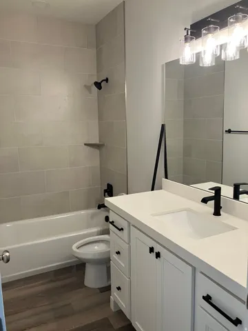 Bathroom with wood-finish flooring, a white vanity with a recessed sink, a white countertop, and a shower/tub combination with light-colored tile surround