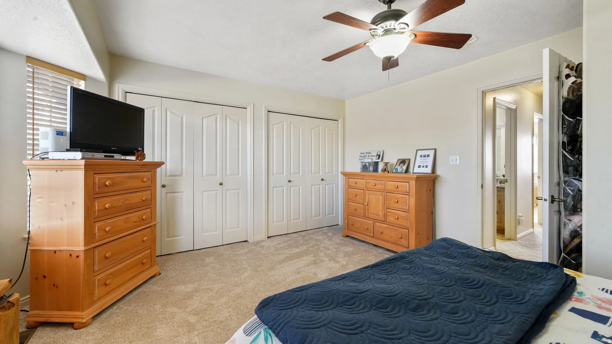 Bedroom with two closets, light carpet, and a ceiling fan