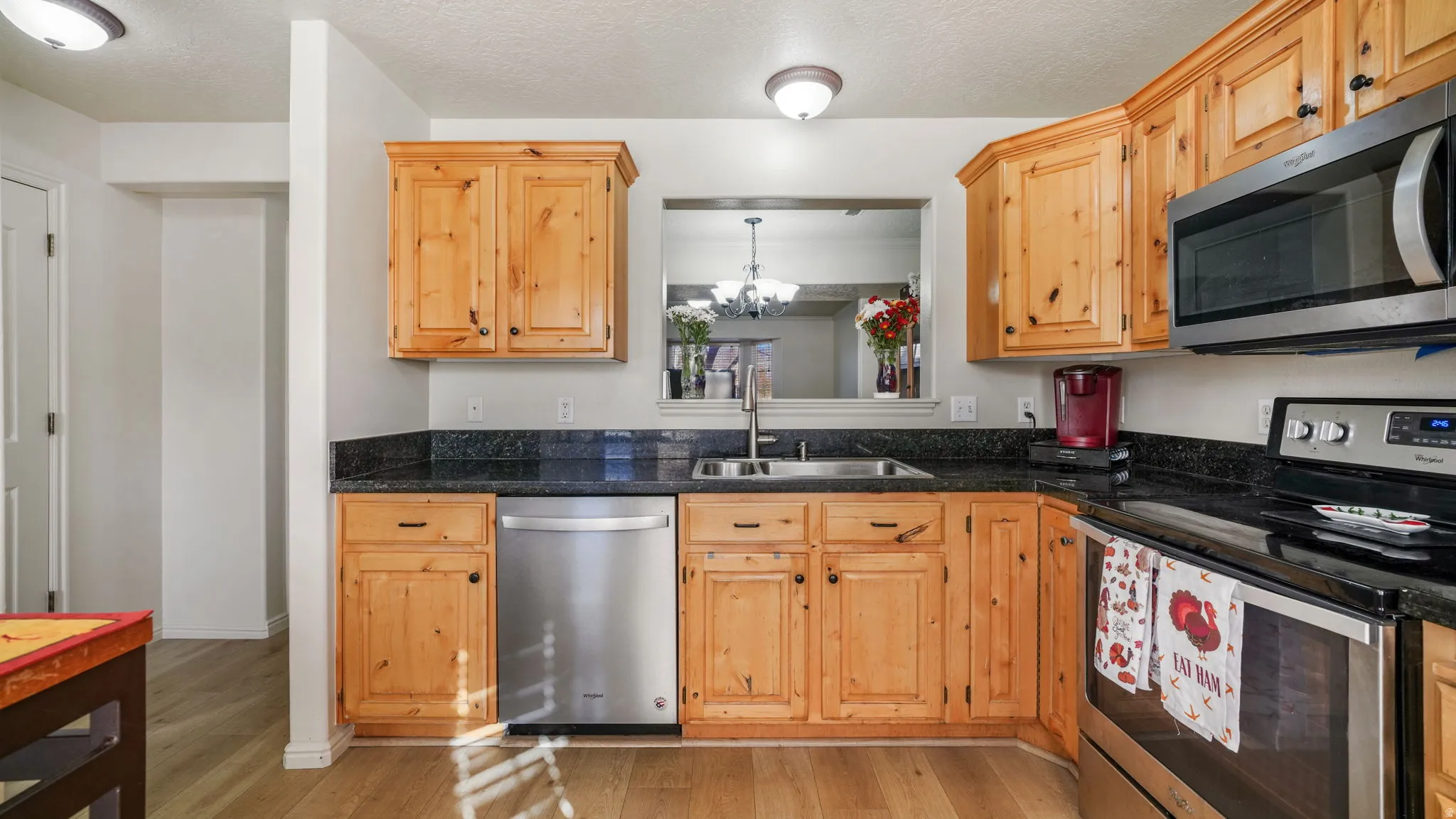Kitchen featuring appliances with stainless steel finishes, light wood finished floors, a textured ceiling, dark stone countertops, and a chandelier