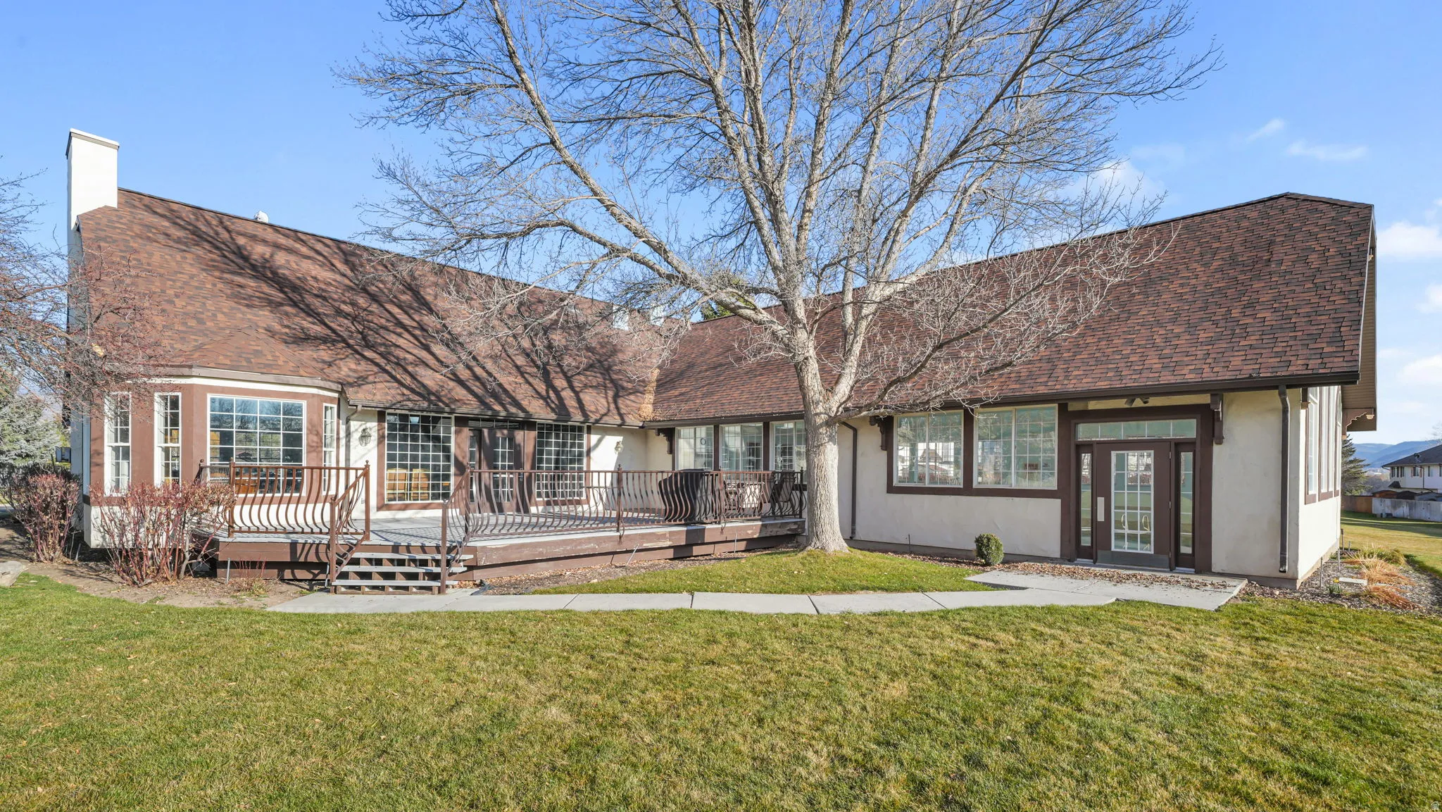 Back of house featuring a lawn, a wooden deck, a chimney, and a shingled roof