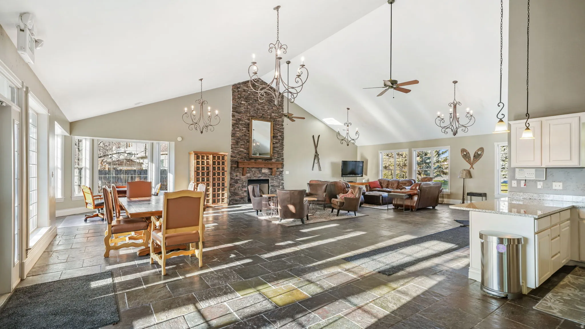 Dining area featuring high vaulted ceiling, a chandelier, a fireplace, stone tile floors, and a ceiling fan