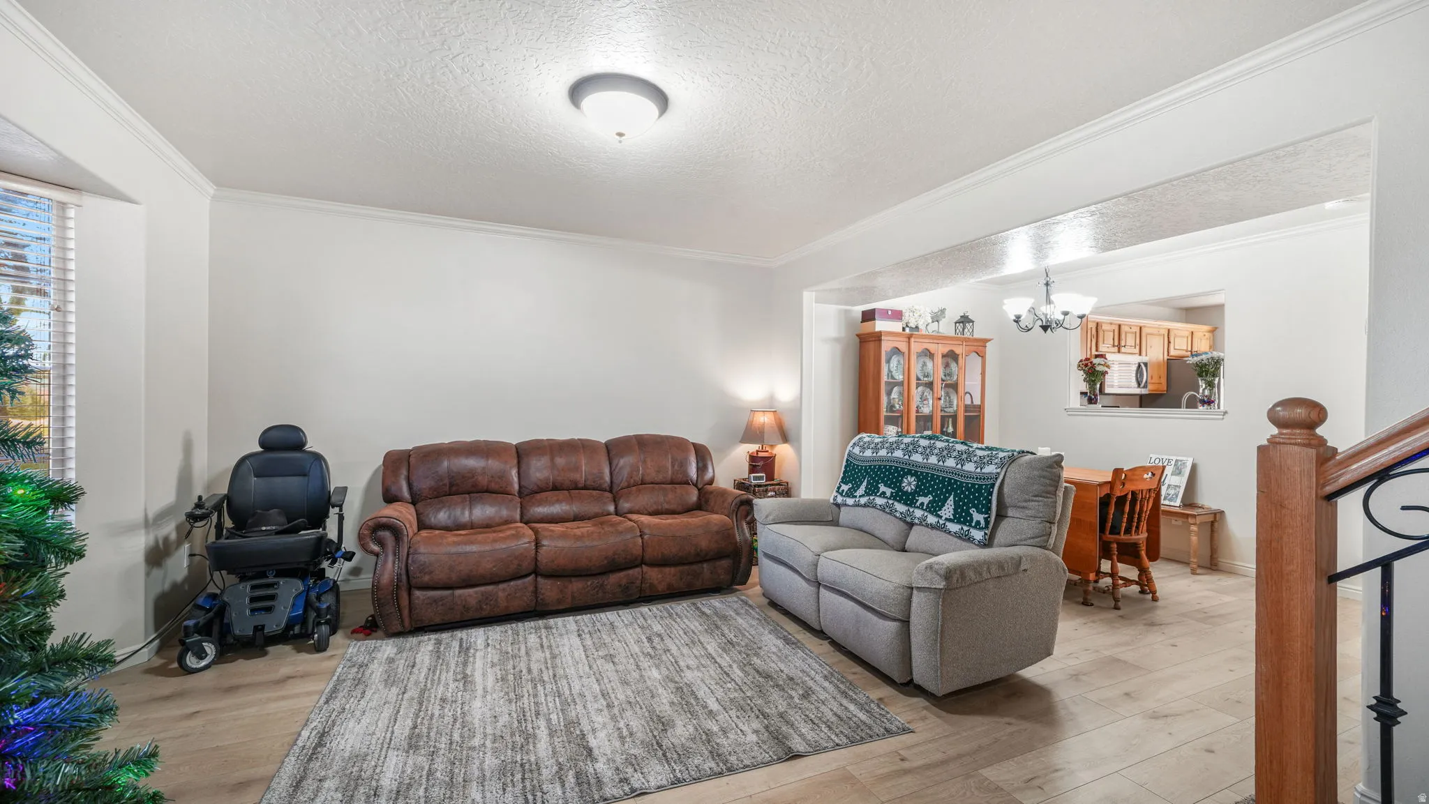 Living room featuring a textured ceiling, crown molding, light wood-style flooring, stairs, and a chandelier