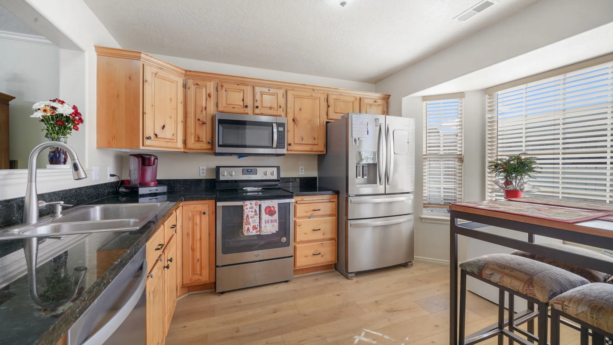 Kitchen with stainless steel appliances, light wood-style flooring, light brown cabinetry, dark stone countertops, and a textured ceiling