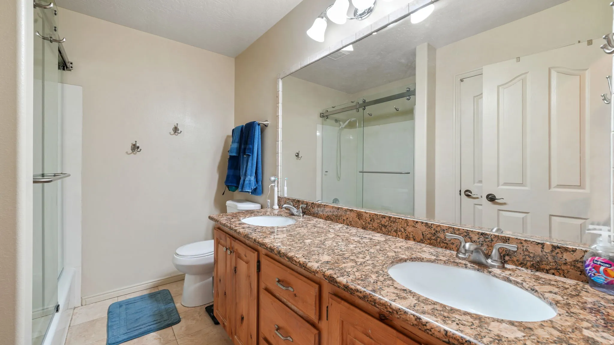 Bathroom with double vanity, a shower stall, and light tile patterned floors