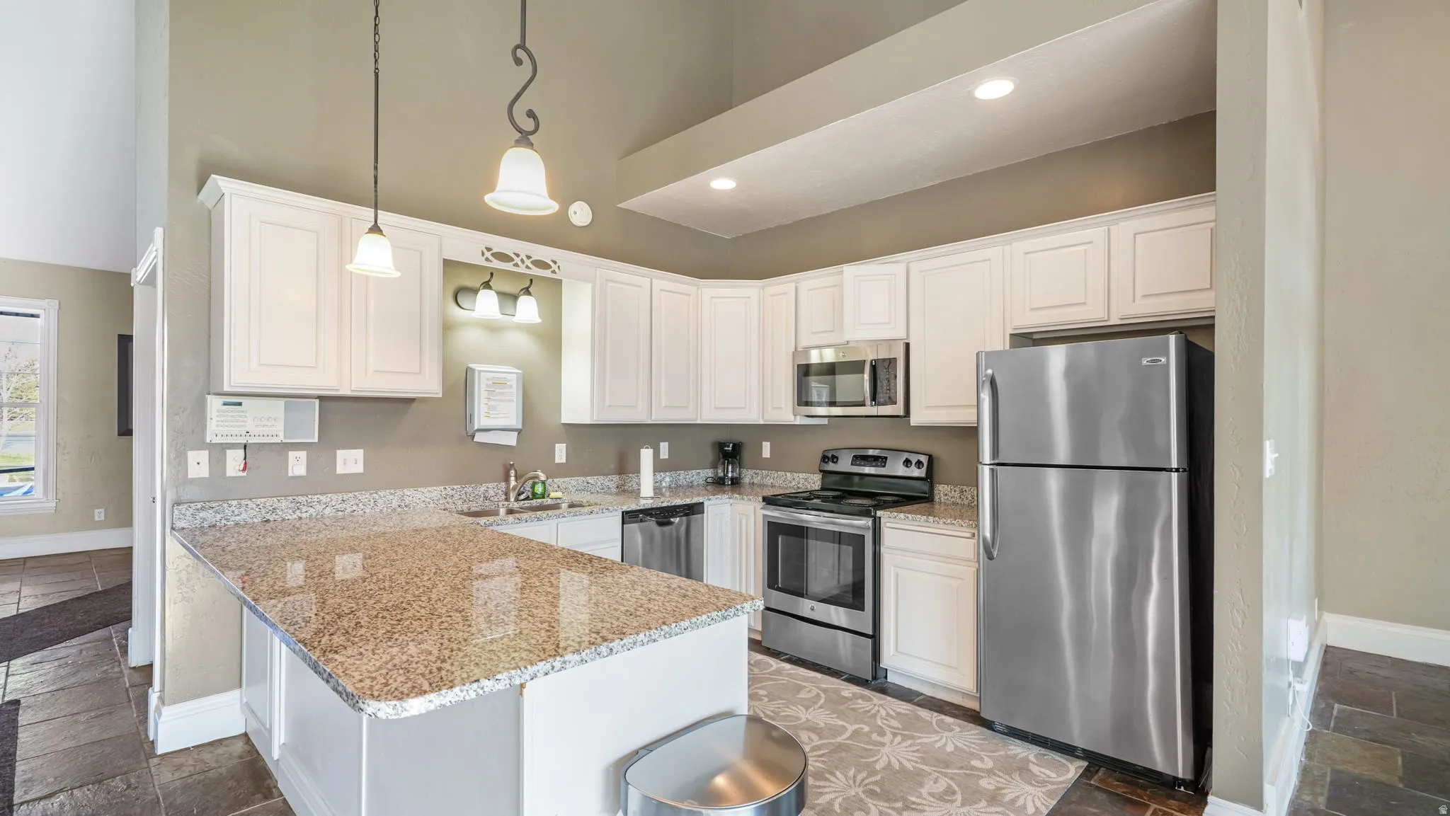 Kitchen featuring stone tile flooring, stainless steel appliances, a peninsula, decorative light fixtures, and light stone countertops