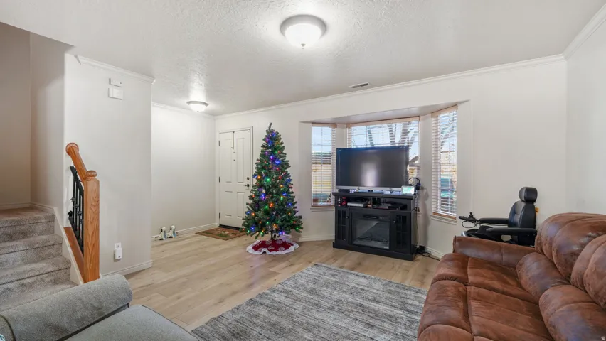 Living area featuring a textured ceiling, light wood-type flooring, stairway, and ornamental molding