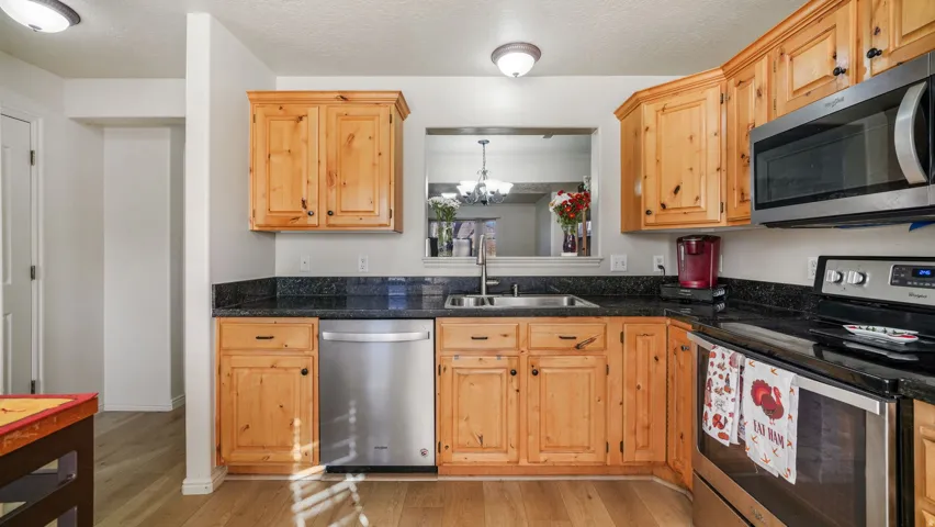 Kitchen featuring appliances with stainless steel finishes, light wood finished floors, a textured ceiling, dark stone countertops, and a chandelier
