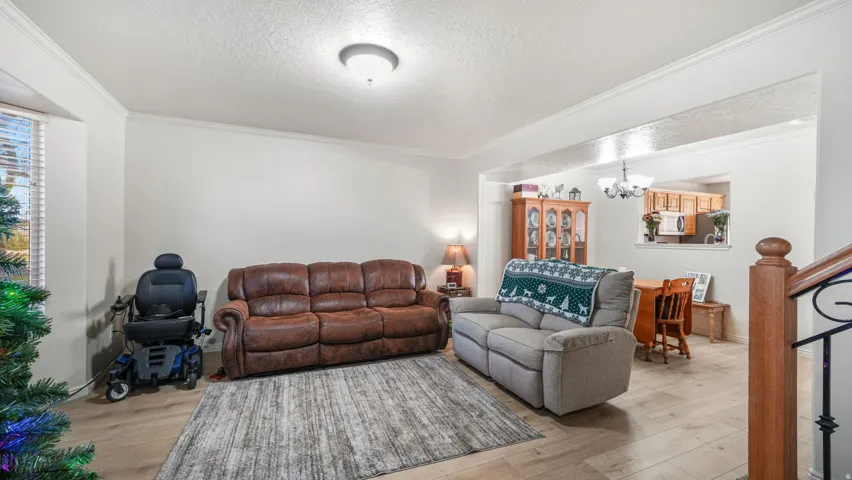 Living room featuring a textured ceiling, crown molding, light wood-style flooring, stairs, and a chandelier