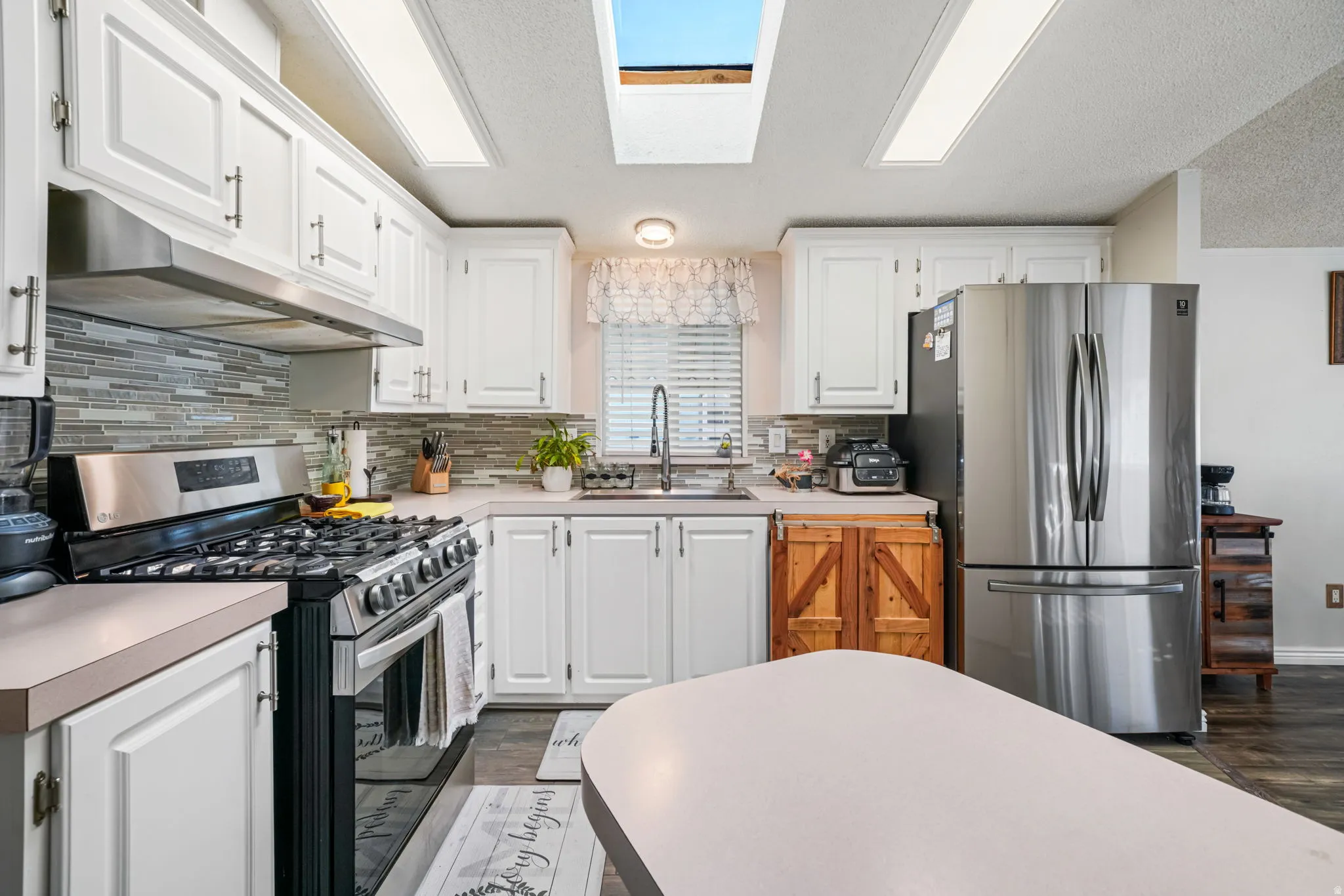 Kitchen with appliances with stainless steel finishes, white cabinets, light countertops, under cabinet range hood, and a textured ceiling