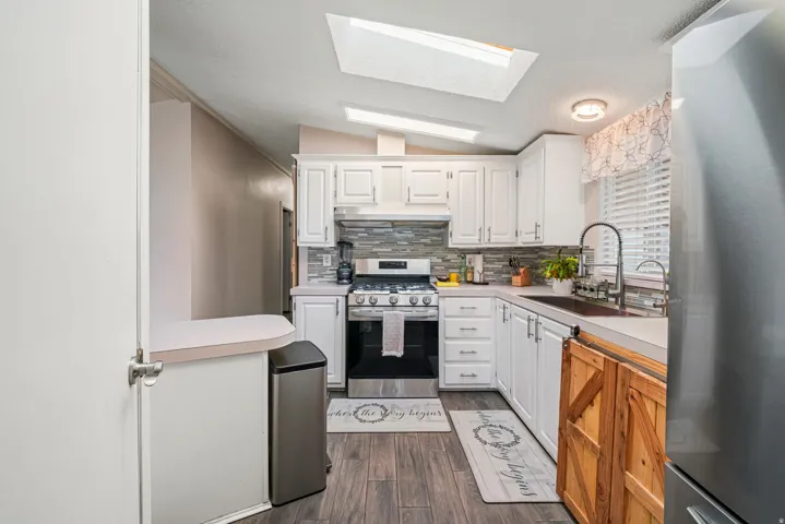 Kitchen featuring light countertops, appliances with stainless steel finishes, white cabinetry, dark wood-style floors, and lofted ceiling