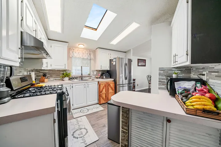 Kitchen with decorative backsplash, appliances with stainless steel finishes, a skylight, and white cabinets