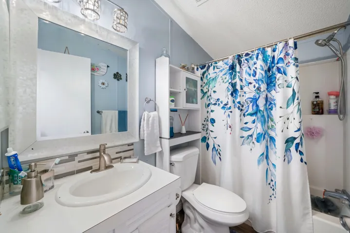Full bathroom with vanity, a textured ceiling, shower / bath combination with curtain, and tasteful backsplash