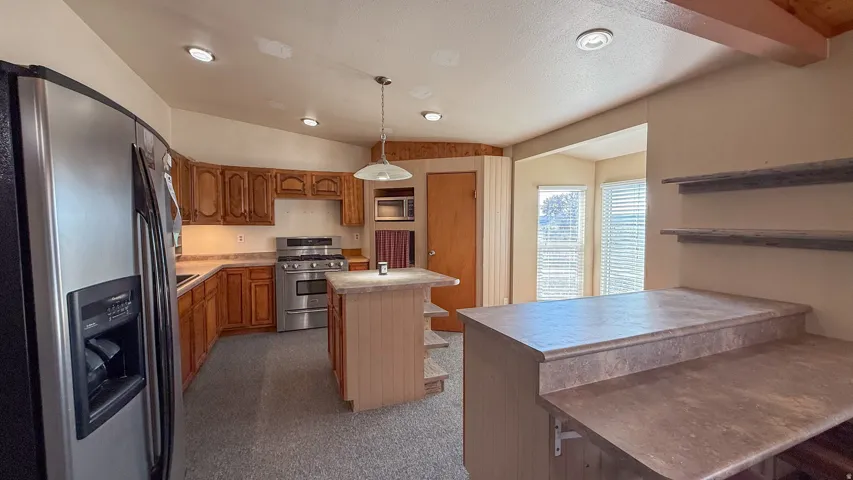 Kitchen with stainless steel appliances, lofted ceiling, a kitchen island, light countertops, and hanging light fixtures